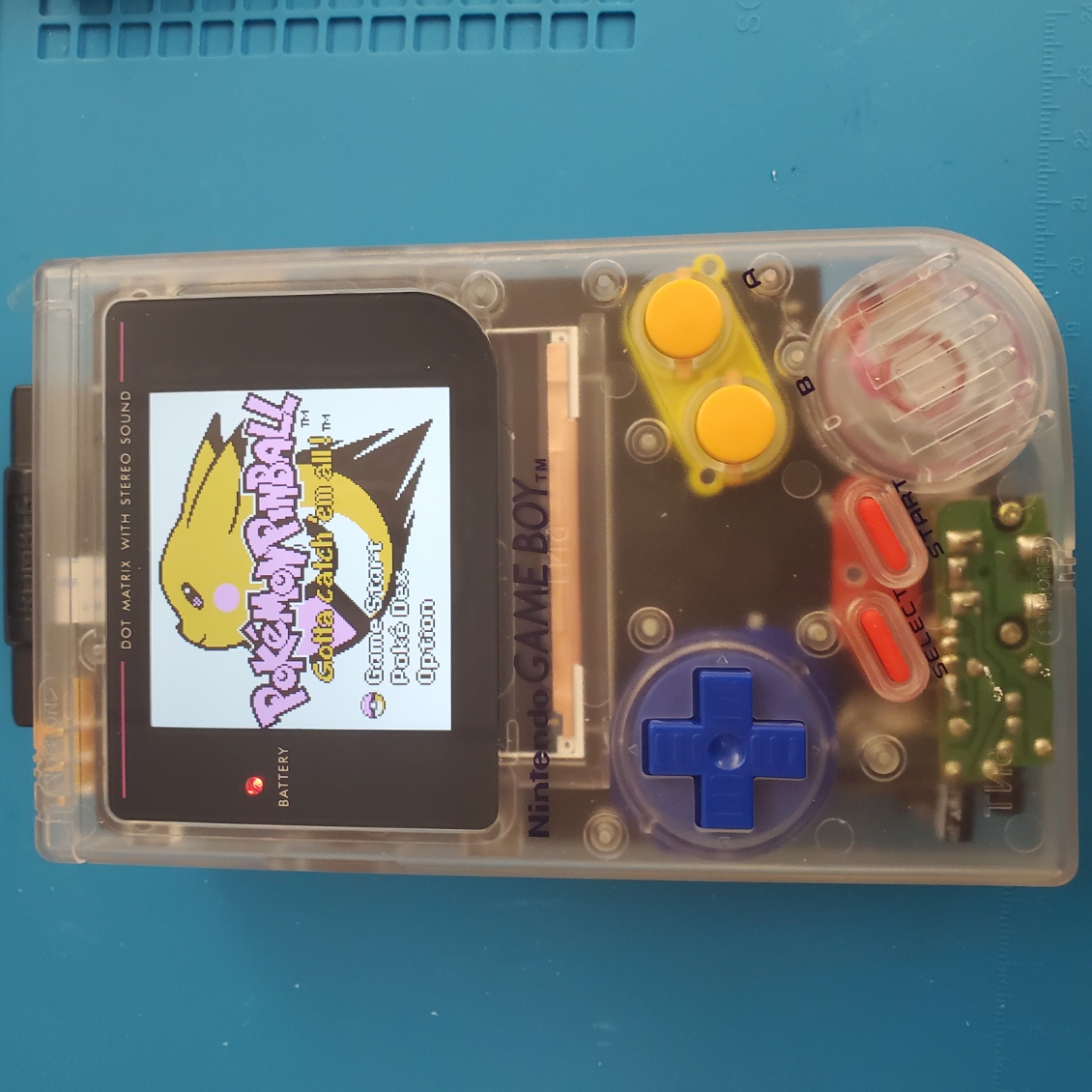 clear gameboy DMG with a visible black board underneath, as well as red, yellow, and blue buttons. pokemon pinball is on screen